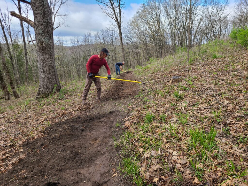A person rakes leaves along a wooded path on the Driftless Trail.