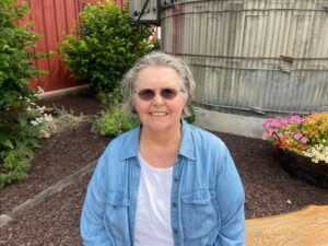 A woman in a blue shirt sits on a wooden bench in front of a red barn.